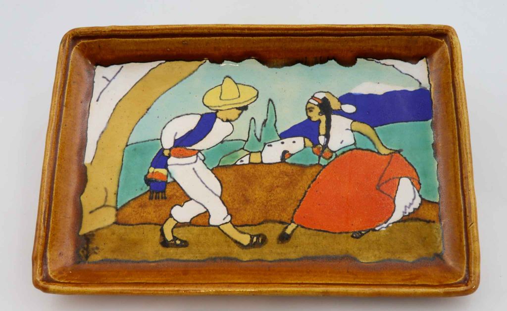 Ceramic tray showing a man and woman dancing together. Behind them in a house on a hill.