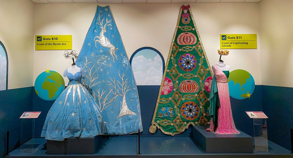 Blue velvet puffy dress and pink/green one-shouldered dress. Both with elaborate trains hung behind them.