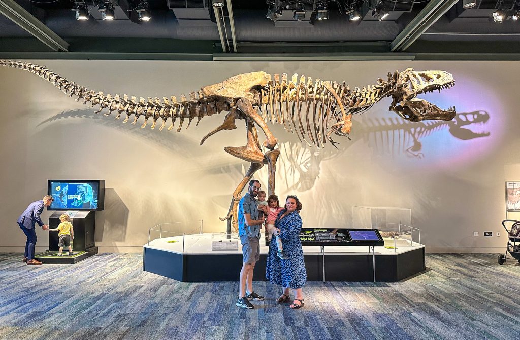 Family of four stands in front of giant Scotty t. rex cast.