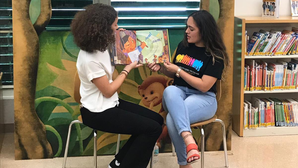 Two people read an illustrated book aloud.