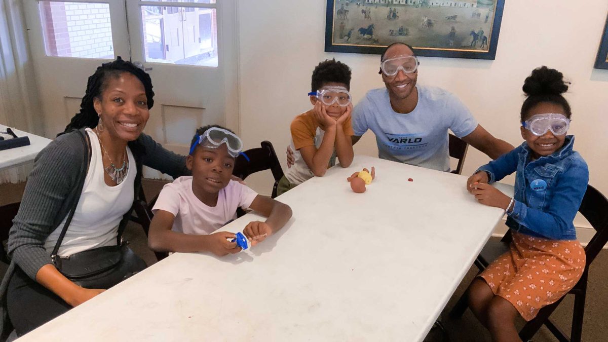 Family of five wearing lab goggles sits around a table.