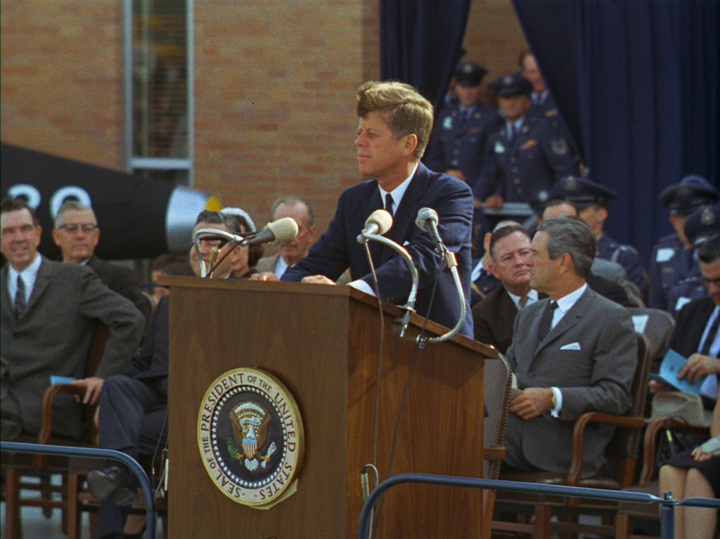 President John F. Kennedy stands behind a lectern.