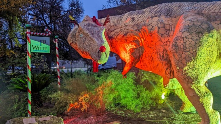 Statue of Arky wearing antlers and red nose under red/green lights.