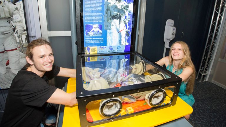 two young adults use space gloves