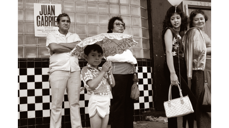 Family standing in front of storefront while child holds umbrella.