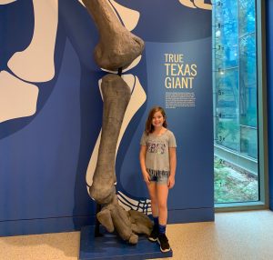 little girl standing next to a dinosaur fossil foot